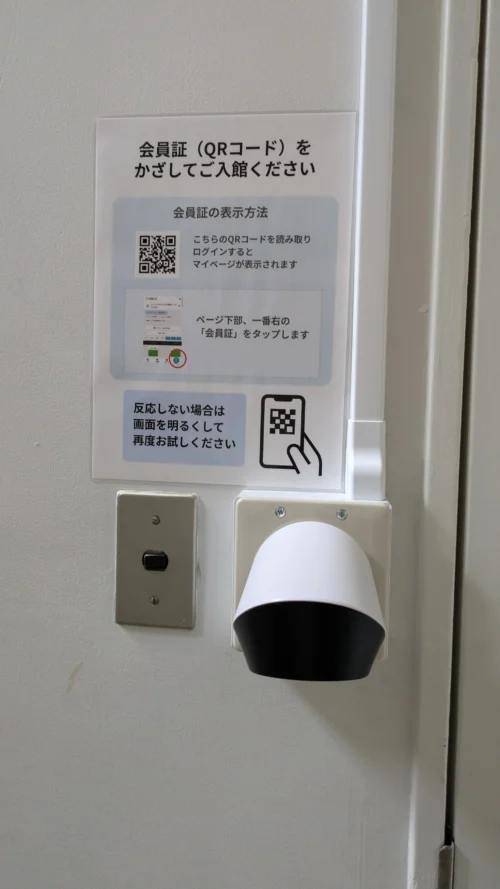 入口ドアのQRコードリーダーと、会員証の表示方法を説明した掲示