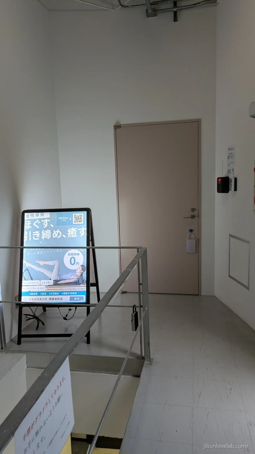 ソエルスタジオ堺筋本町店がある4階の踊り場。店舗の扉とA看板、壁のカードリーダー
